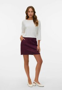 Witte top met lange mouwen gecombineerd met een pruimenrood kort rokje met zijzakken, aangevuld met witte blokhakken. Eenvoudig en strak ontwerp.