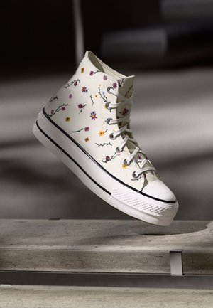 Hochschnitt-Sneaker mit einem cremefarbenen Canvas-Obermaterial, das mehrfarbige Blumenstickerei aufweist, einer weißen Gummisohle und schwarzen Akzenten.