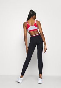 Zestaw sportowy składający się z czerwonego i szarego biustonosza sportowego z regulowanymi ramiączkami oraz czarnych legginsów. Materiał jest gładki z dopasowanym krojem.