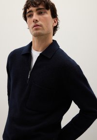 Maglione navy a collo zipper, realizzato in morbido tessuto, con taschino sul petto e colletto strutturato. Texture liscia e forma aderente.