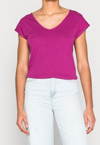 Fuchsia kortärmad T-shirt med V-hals i mjukt bomullsmaterial, något avslappnad passform, parat med ljus tvättade högmidjade jeans.