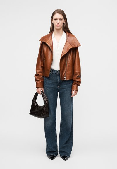 Καφέ δερμάτινο τζάκετ cropped με φαρδύ γιακά, συνδυασμένο με μπλε ψηλόμεσα τζιν και μία μικρή σκούρα πλεκτή τσάντα.
