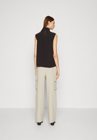 Top nero senza maniche con colletto alto, abbinato a pantaloni cargo beige larghi con tasche laterali e vestibilità comoda.