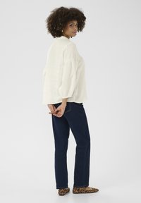 Blusa bianca in lino con maniche a sbuffo, abbinata a jeans blu scuro e ballerine con stampa leopardata. L'outfit presenta una vestibilità comoda e un design semplice.