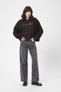 Felpa nera corta con la scritta "FEMME" in lettere testurizzate, abbinata a jeans grigi larghi e scarpe con plateau nere. Look semplice e casual.