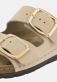 Sandalo beige in camoscio con due larghe fascette, dotato di fibbie in metallo color oro. Plantare sagomato con suola in gomma scura, per comfort e supporto.