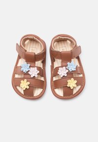 Καφέ σανδάλια για νήπια με τρεις λουριά και πολύχρωμες διακοσμήσεις λουλουδιών σε μπλε, ροζ και κίτρινο, σε λευκό φόντο.