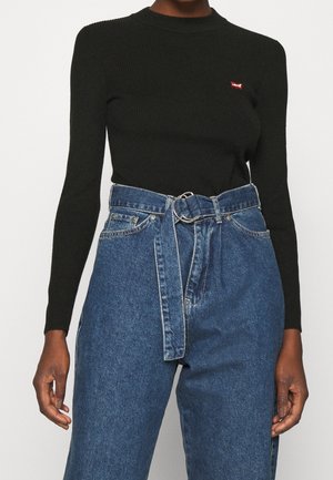 Osoba nosząca czarną, prążkowaną bluzkę z długim rękawem z małym czerwonym logo oraz niebieskie jeansy z wysokim stanem i pasującym paskiem z denimu.