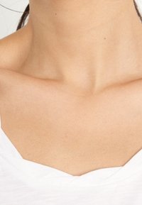 Bílé tričko s krátkými rukávy a výstřihem do V. Hladká textura, vrstvená tkanina kolem výstřihu, těsně obepínající oblast klíční kosti.