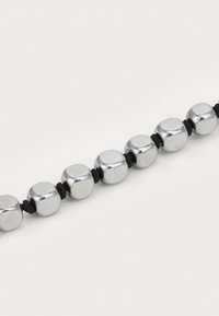 Sølvmetalperler i geometrisk form, trukket på sort snor, med en glat reflekterende overflade og mat finish på nogle perler.