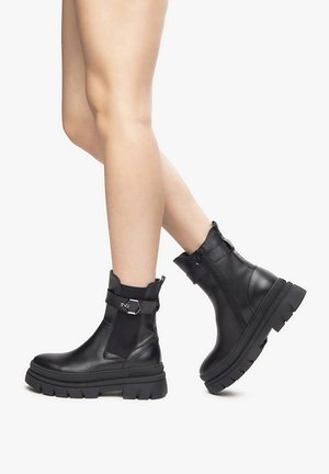 Black leather ankle boots with a chunky sole, elastic side panels, and a decorative metal buckle. Smooth texture with a sleek design.