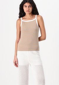 Beige og hvit stripete tanktop med tykke hvite stropper, parret med hvite, løst strikkede vide bukser. Teksturen er rillet og pustende.