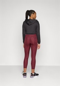 Black hooded crop top, maroon patterned leggings, and black athletic shoes with pink accents, showcasing a fitted design and textured fabric.