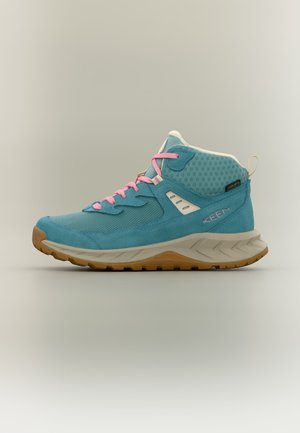 Chaussure de randonnée bleue avec lacets roses, semelle beige et marron, et matériau en mesh respirant, posée sur un fond neutre.