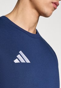 Μπλε ναυτικό βαμβακερό t-shirt με στρογγυλή λαιμόκοψη και κοντά μανίκια. Διαθέτει λευκό κεντημένο λογότυπο με τρεις ρίγ ες στην αριστερή πλευρά του στήθους.