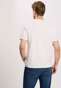 Biała koszulka z krótkim rękawem, wykonana z bawełny, z klasycznym okrągłym dekoltem. Noszona z niebieskimi dżinsami, prezentująca prosty, czysty design.