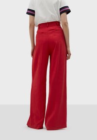 Red, high-waisted wide-leg trousers made of a smooth fabric. Features a back zipper and two rear pockets, with a clean, tailored finish.