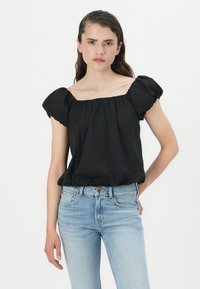 Black puff-sleeve top with a square neckline, made of soft fabric; paired with light blue fitted jeans, showcasing a relaxed style.