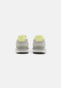 Baskets grises et blanches avec une tige texturée, présentant un accent jaune au niveau du talon et une semelle rembourrée pour le soutien.