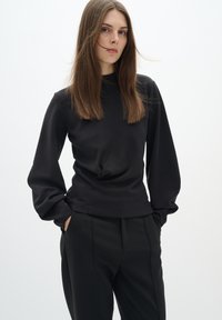 Black long-sleeve top with a round neckline, smooth texture, and relaxed fit, paired with tailored black pants. Simple, monochrome design.