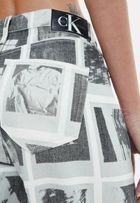 Džinsai su fotografiniu raštu juodai baltos spalvos ir iškilniu Calvin Klein Jeans žymėjimu ant juosmens.