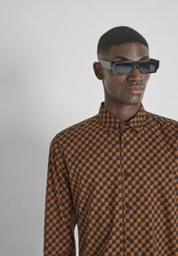Bruin en zwart gestreepte shirt met een geometrisch ontwerp, knoopsluiting en een kraag. De stof heeft een gladde textuur.