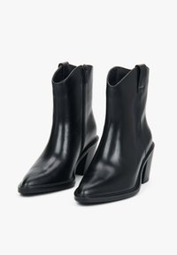 Czarne skórzane botki za kostkę z ostrymi noskami, bocznymi zamkami błyskawicznymi, pętlami do zakupu i grubymi, prostokątnymi obcasami na białym tle.