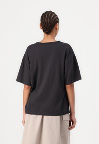 Svart oversized t-skjorte laget av bomull, med korte ermer og rund hals. Glatt tekstur med sømmer.