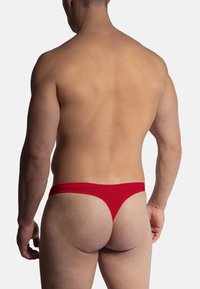 Rode string onderbroek, gladde stof, minimale bedekking en een smalle tailleband. Het ontwerp accentueert de vorm van het lichaam.