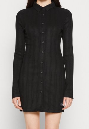 Black ribbed long-sleeve button-up dress with a collar, mid-thigh length, and small logo patch near the hem on the left side.