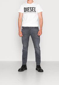 Valkoinen t-paita, jossa on rohkea musta "DIESEL"-painatus, yhdistetty tummanharmaisiin farkkuihin ja mustiin nauhakenkäsaappaisiin. Yksinkertainen muotoilu, vähäiset yksityiskohdat.