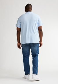 Lyseblå polo med klassisk krave, korte ærmer og afslappet pasform, kombineret med mørkeblå jeans og hvide sneakers.