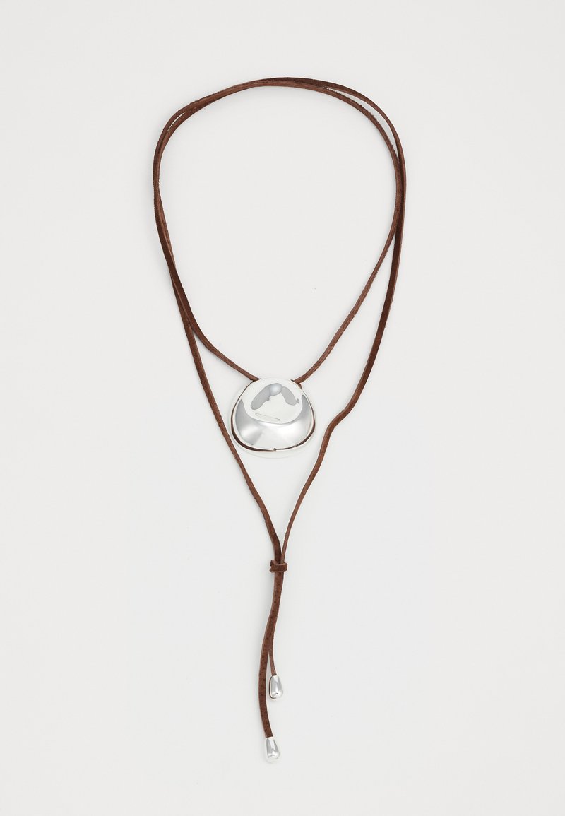 Collana in pelle marrone con un pendente in argento caratterizzato da una forma organica e arrotondata, con una superficie liscia, accentuata da due tappi in argento alle estremità.