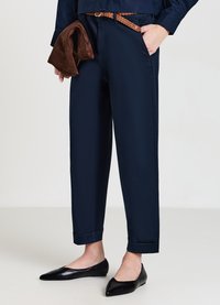 Pantaloni blu navy con una vestibilità comoda, dotati di una cintura intrecciata marrone, abbinati a ballerine nere a punta. Texture liscia e orli arrotolati.