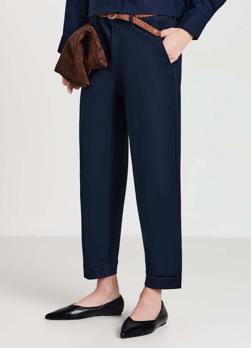 Pantaloni blu navy con una vestibilità comoda, dotati di una cintura intrecciata marrone, abbinati a ballerine nere a punta. Texture liscia e orli arrotolati.