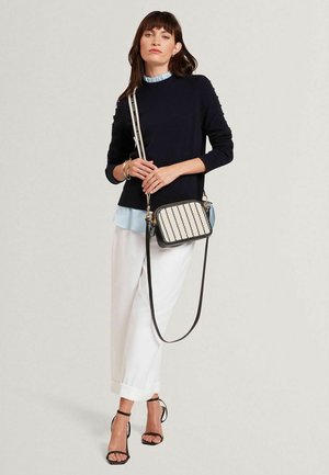 Marineblauwe trui, lichtblauw overhemd met kraag, witte broek met wijde pijpen en zwarte sandalen met bandjes. Zwarte crossbodytas met een crème gestreept design.