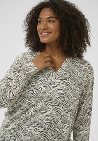 Ilgi piedurkņu, V veida kakla tops krēmkrāsā ar melnām zebru svītrām; mīksts, teksturēts audums ar brīvu piegriezumu un detalizētiem aprocēm.