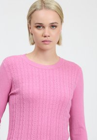 Suéter de punto rosa con un patrón de cable vertical texturizado y cuello redondo. La tela parece suave y ligera. Manga larga.