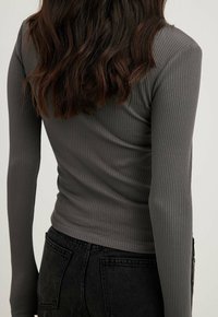 Maglia a maniche lunghe a coste in tessuto grigio scuro, con un design aderente e un collo alto, abbinata a jeans neri con una finitura texture.