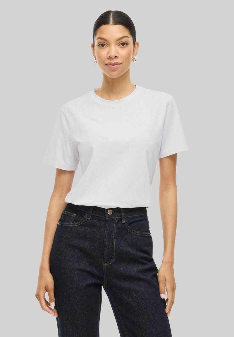 Vit bomullströja med korta ärmar, rund halsringning, slät textur, kombinerad med mörkblå högmidjade jeans. Enkel design, inga mönster.