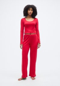 Haut rouge à manches longues avec texture côtelée et bords festonnés, associé à un pantalon large assorti. Tissu doux et léger, design décontracté.