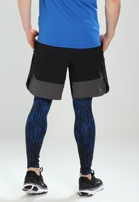 Černé šortky s šedými akcenty v kombinaci s modrými legínami se vzorem. Legíny mají texturovaný design. Oblečeno s černými sportovními botami.