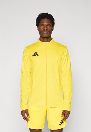 Gele sportieve trainingspak met ritsvest en bijpassende korte broek. Voorzien van zwarte adidas-logo accenten. Soepele, lichte stof.