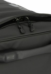 Sac noir en matériau synthétique lisse, avec une fermeture éclair dotée de deux tirettes noires et une poignée texturée sur le côté.