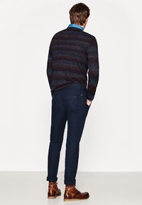 Czarny sweter w paski w niebieskich i burgundowych odcieniach, zestawiony z ciemnymi dopasowanymi spodniami i brązowymi skórzanymi butami, widok z tyłu.