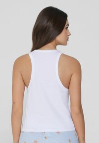 Camiseta de algodón blanca sin mangas con un escote redondeado y agujeros para los brazos caídos, que muestra una textura suave y ligera.