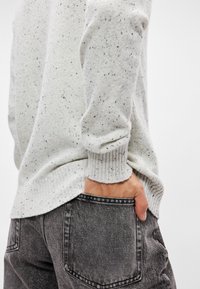 Ανοιχτό γκρι πλεκτό πουλόβερ με σπιρτόζα υφή, ριγέ μανσέτες, συνδυασμένο με σκούρο γκρι τζιν παντελόνι, που διαθέτει πίσω τσέπη και ξεθωριασμένη απόχρωση.