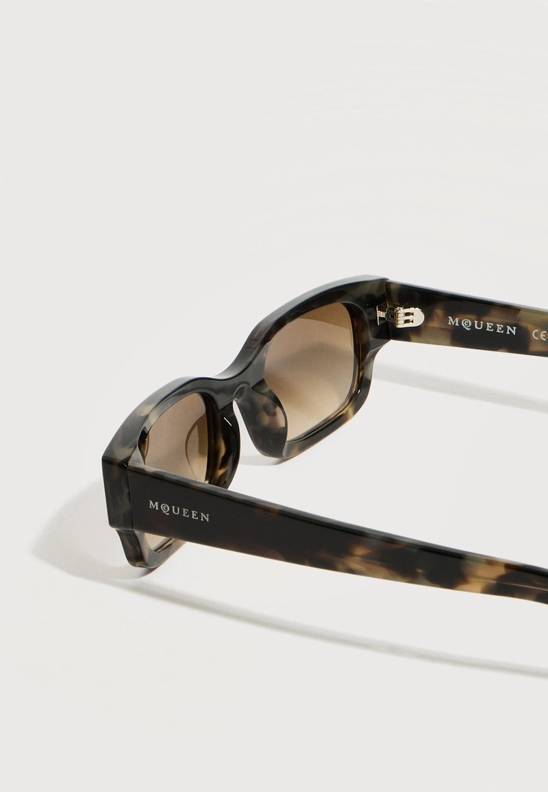Lunettes de soleil à motif écaille avec des verres rectangulaires teintés marron et logo McQueen sur les branches noires.