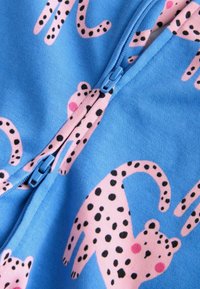 Blå stofbeklædning med lynlås, dekoreret med pink leoparder og sorte pletter, blød tekstur. Designet fremhæver legende dyremønstre.