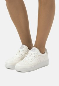 Weiße Leder-Sneaker mit perforierter Zehenpartie, gepolsterter Zunge und strukturiertem Mittelsohle. Merkmale des minimalistischen Designs und graue Akzenten an der Ferse.